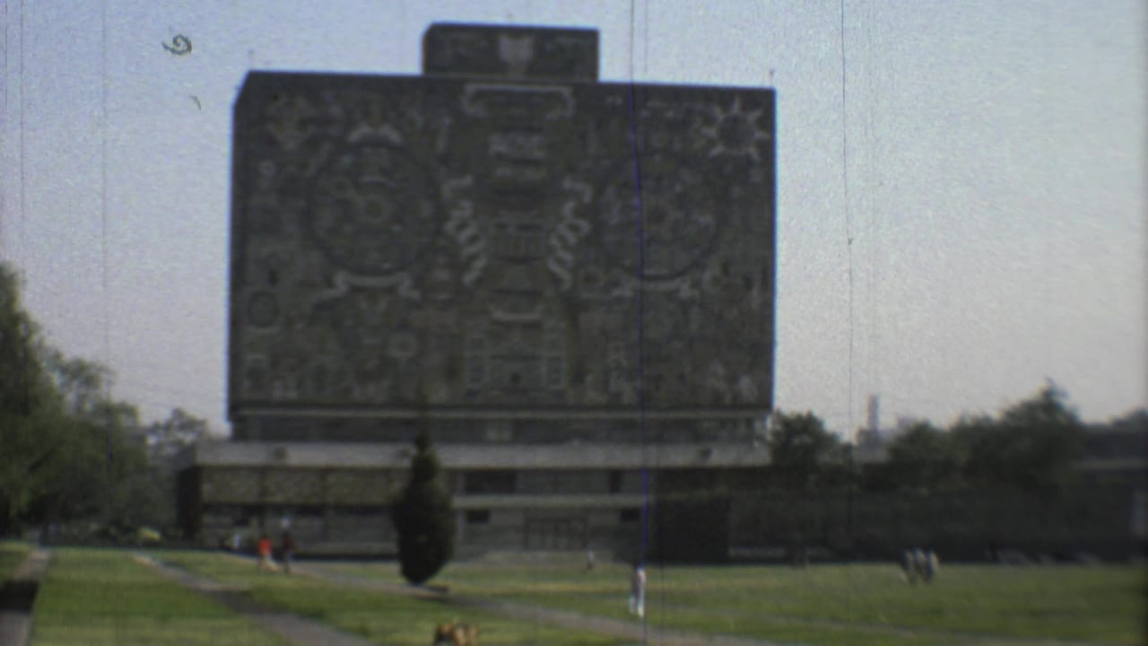 1973 Mexico City home-movie view of a mosaic-covered landmark seen across lawn, paths, and distant park visitors.