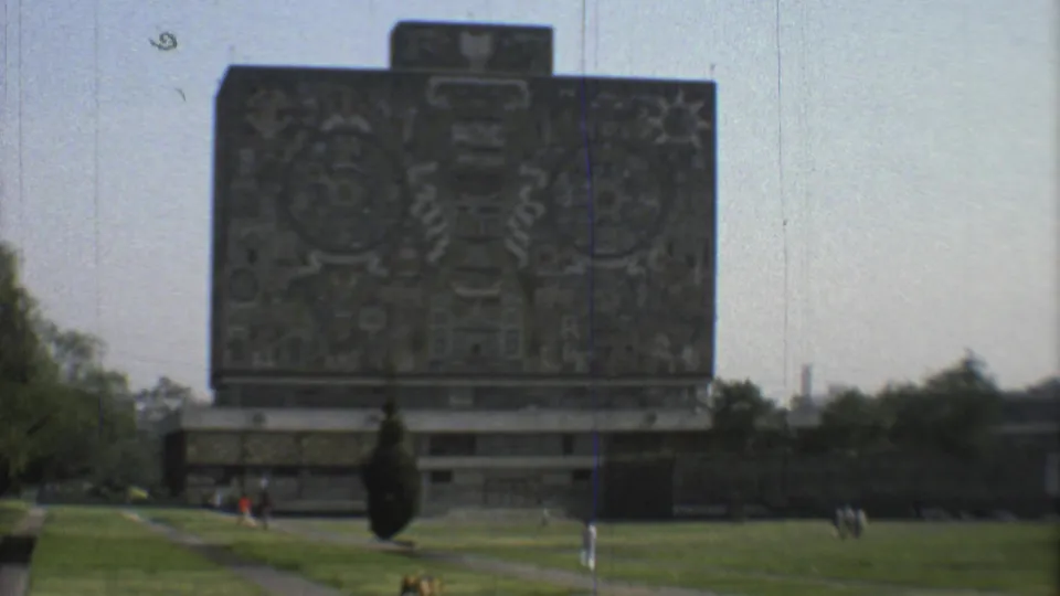 1973 Mexico City home-movie view of a mosaic-covered landmark seen across lawn, paths, and distant park visitors.