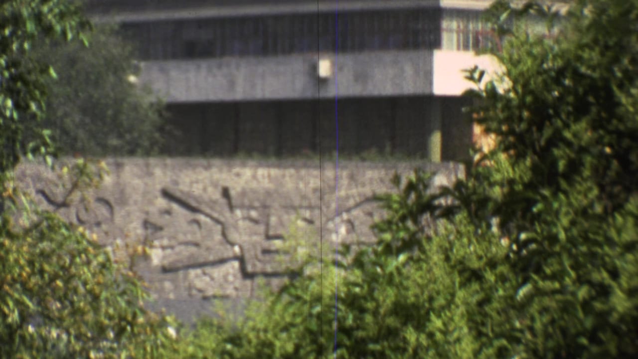 End frame of the 1973 Mexico City zoom showing the relief wall, dark window strip, and surrounding trees at closer range.