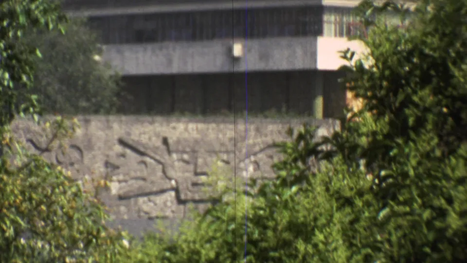 End frame of the 1973 Mexico City zoom showing the relief wall, dark window strip, and surrounding trees at closer range.