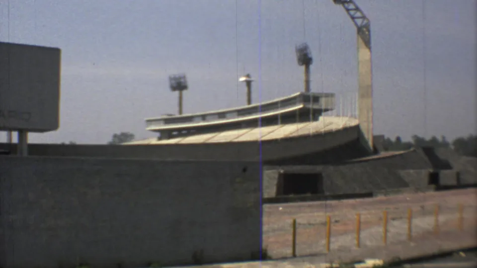 1973 Mexico City exterior view of a concrete stadium-like structure with floodlights, roadside posts, bare trees, and a crane nearby.