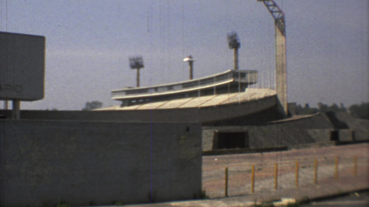 1973 Mexico City 8mm frame showing Estadio Olimpico Universitario exterior with concrete walls, curved seating edge, and floodlight towers.