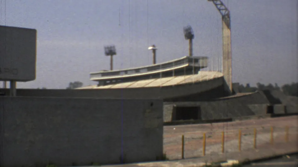1973 Mexico City 8mm frame showing Estadio Olimpico Universitario exterior with concrete walls, curved seating edge, and floodlight towers.