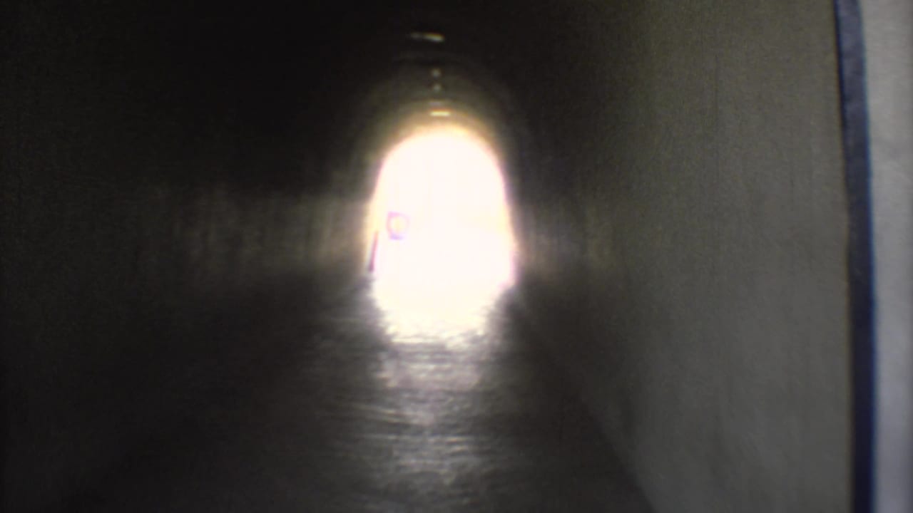 1973 Mexico City 8mm frame inside a dark tunnel, looking toward a bright exit light over reflective pavement.