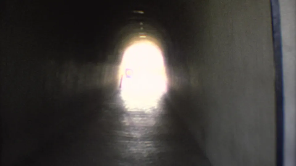 1973 Mexico City 8mm frame inside a dark tunnel, looking toward a bright exit light over reflective pavement.