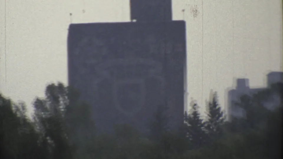 A distant tall building rises behind roadside trees in hazy 1973 Mexico City footage.