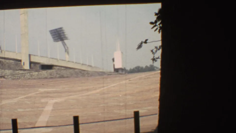 1973 Mexico City 8mm view across an empty dirt stadium surface toward concrete bleachers and a large floodlight array.