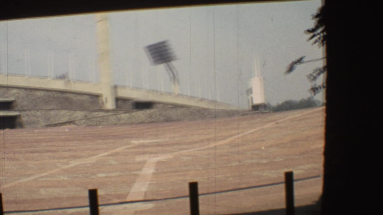 1973 Mexico City frame of an empty stadium or track area with concrete seating, floodlights, foreground posts, and dark side framing.