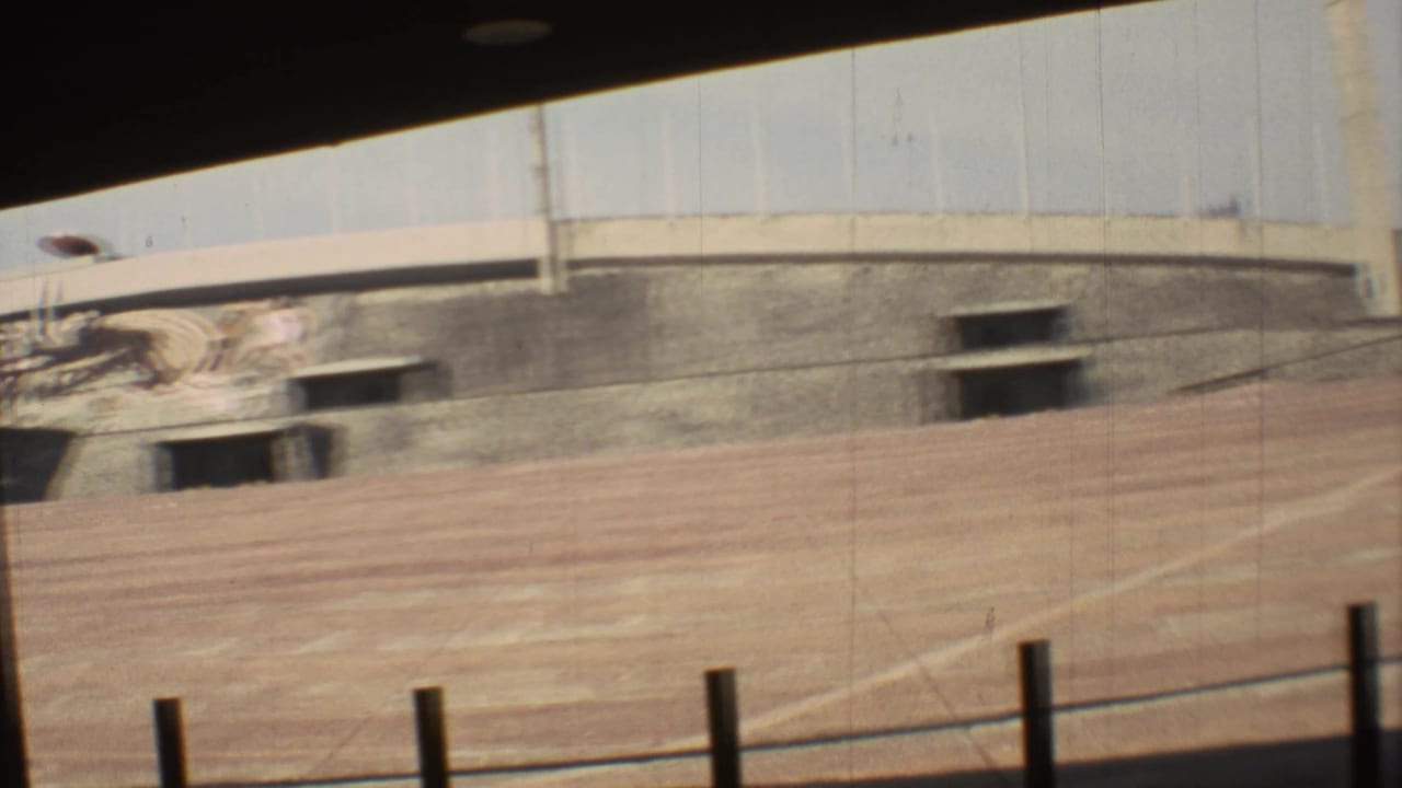 1973 Mexico City 8mm frame with motion blur across an empty dirt track, concrete grandstand wall, and dark rectangular openings.