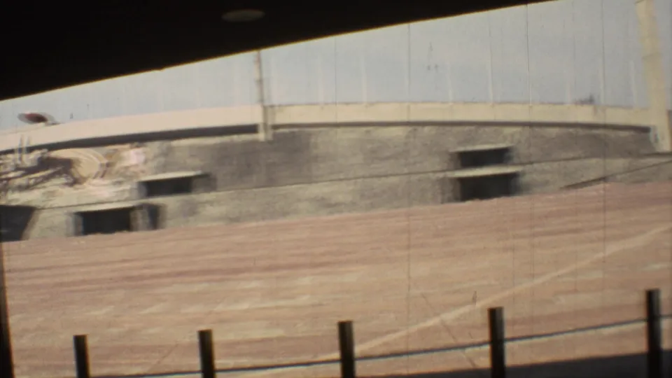1973 Mexico City 8mm frame with motion blur across an empty dirt track, concrete grandstand wall, and dark rectangular openings.