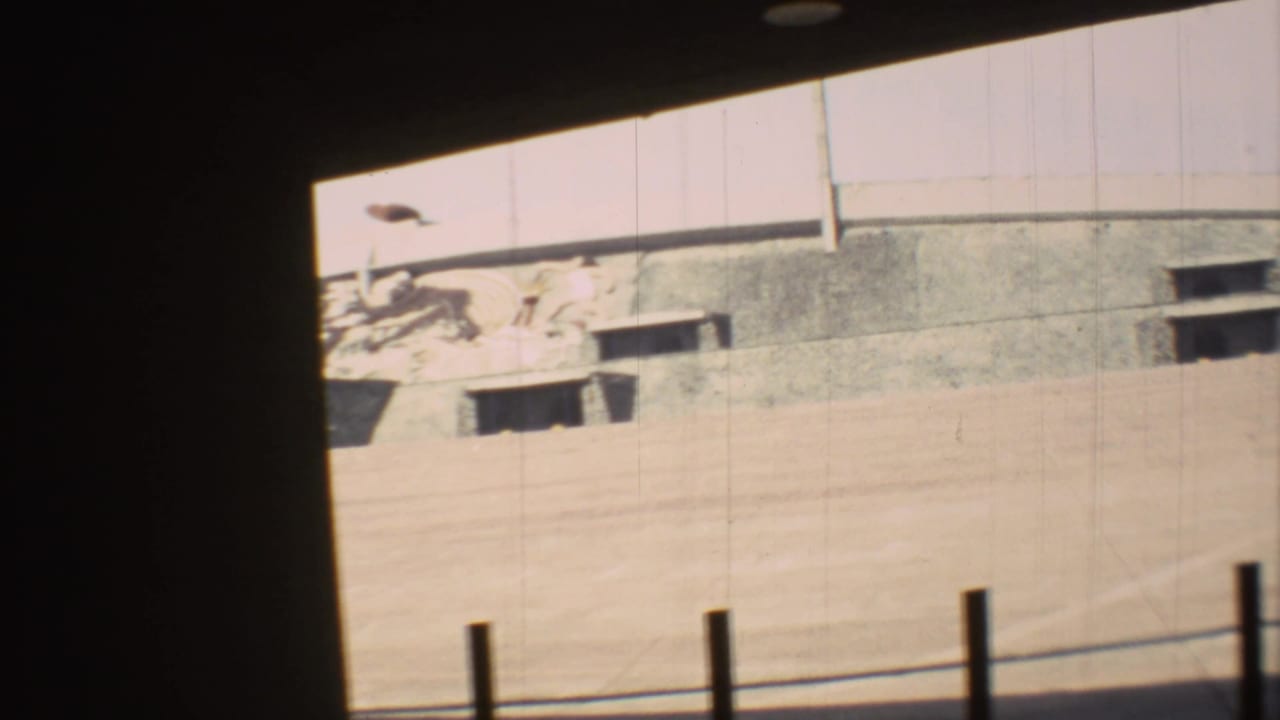 Overexposed 1973 Mexico City stadium frame showing the empty dirt track, concrete wall, openings, and heavy 8mm frame shadow.