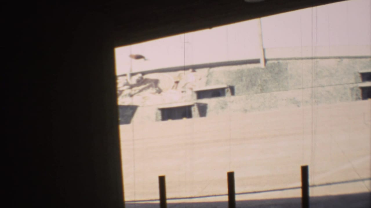 Dark foreground framing a sunlit exterior wall with mural detail and vertical posts.
