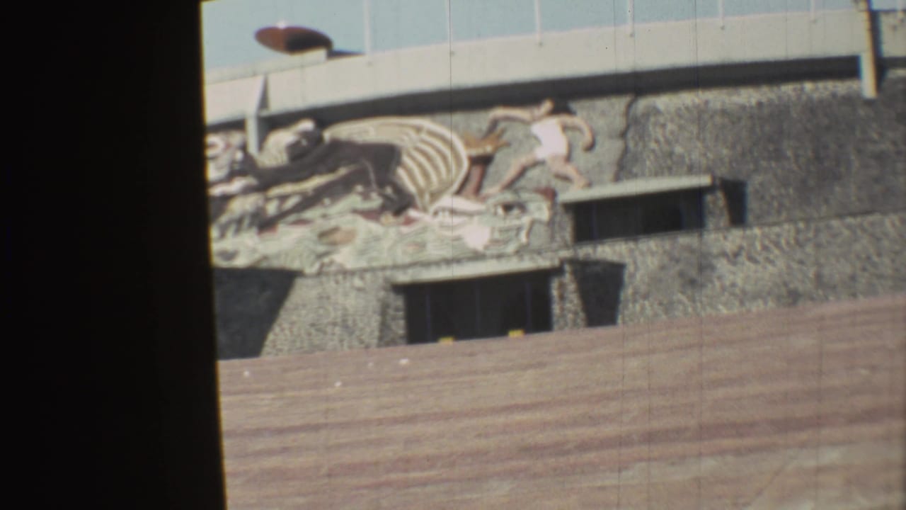 1973 Mexico City 8mm view of a textured wall mural above a wooden barrier, with a turquoise van partly visible at the right edge.