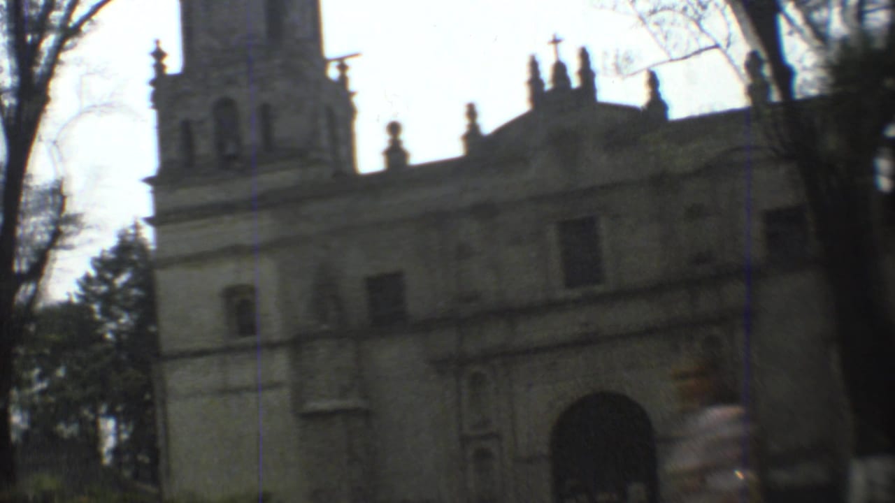 A Mexico City church exterior with tower, arched entry, and trees, captured in soft handheld 8mm footage from 1973.