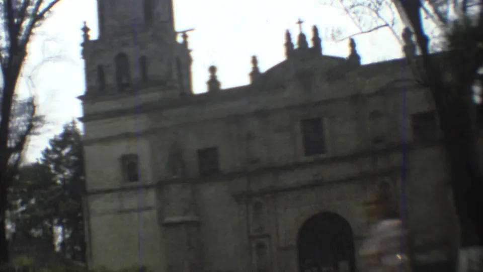 A Mexico City church exterior with tower, arched entry, and trees, captured in soft handheld 8mm footage from 1973.