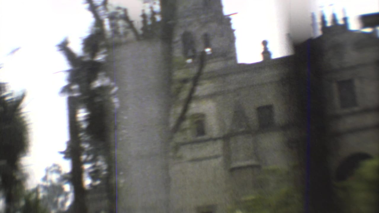 Handheld 8mm frame with motion blur as the camera passes a church tower and facade behind trees in Mexico City.