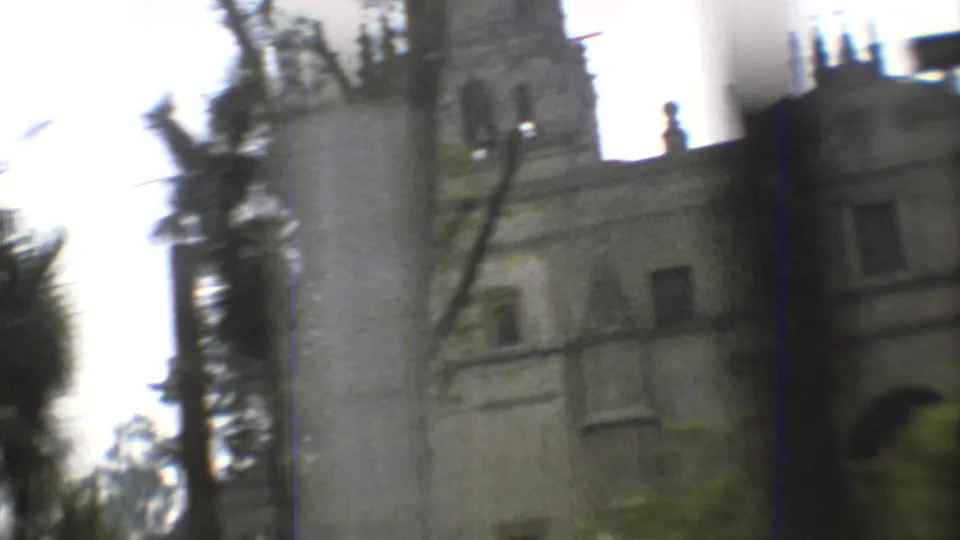 Handheld 8mm frame with motion blur as the camera passes a church tower and facade behind trees in Mexico City.