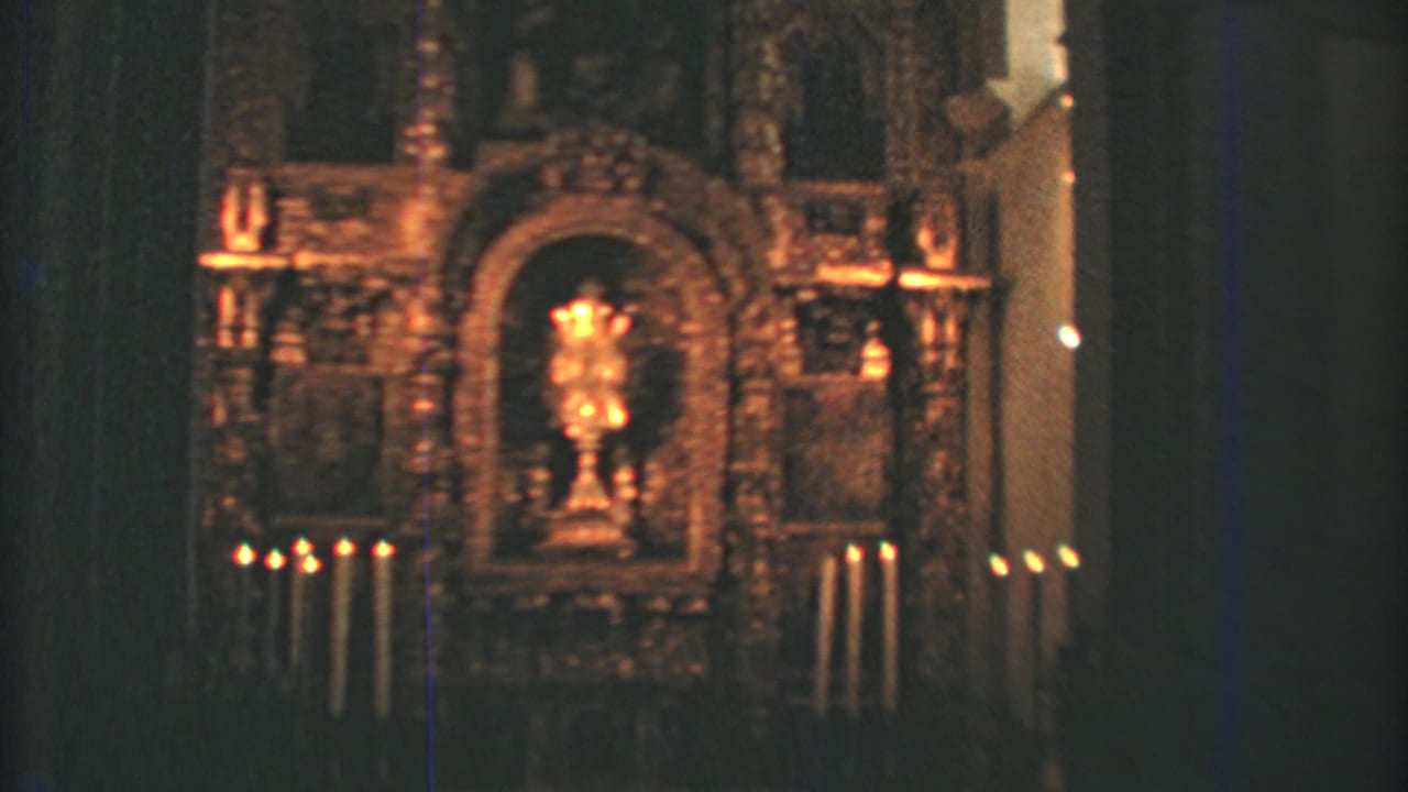 1973 8mm frame of a Mexico City church altar, with rows of candles and a central religious object in soft focus.