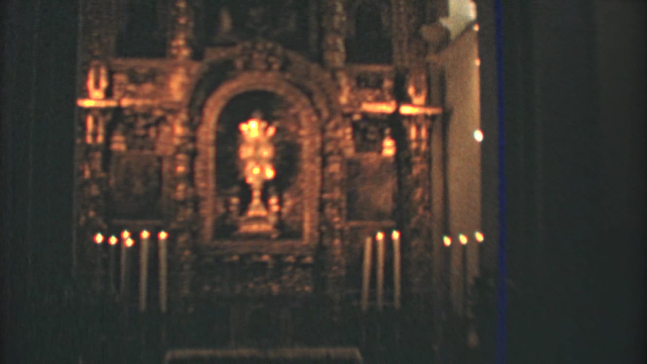 Candlelit Mexico City church altar shown in a steady home-movie view, framed by dark walls and warm gilded detail.