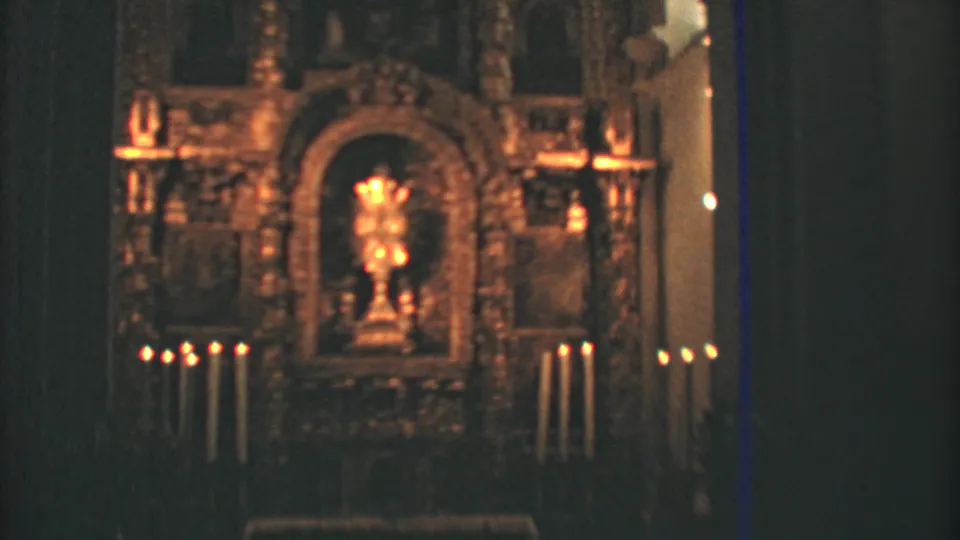 Candlelit Mexico City church altar shown in a steady home-movie view, framed by dark walls and warm gilded detail.
