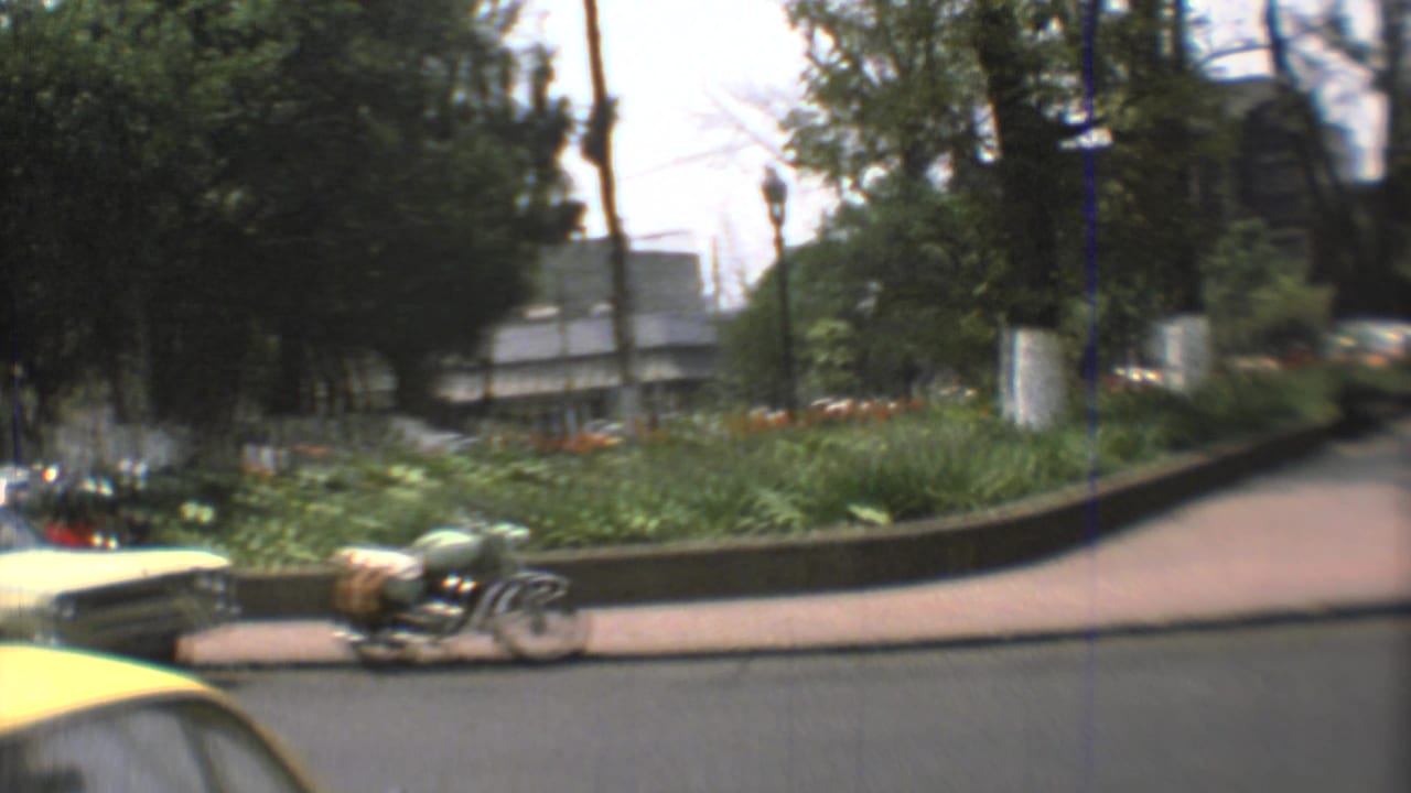 1973 Mexico City street view with a motorcycle near a planted median, tall trees, and part of a yellow car at the curb.