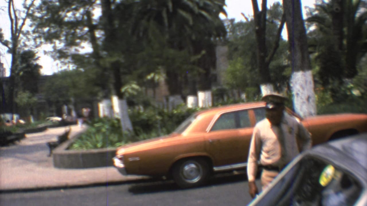 1973 Mexico City street view with a uniformed traffic officer near an orange sedan and a yellow car at the edge of frame.