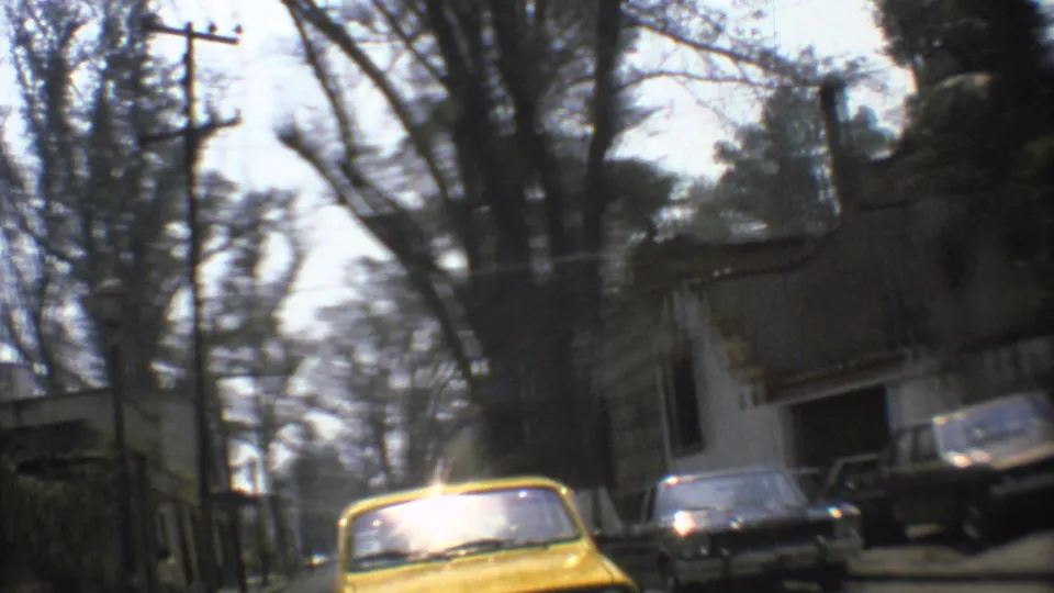 1973 Mexico City street seen from a moving vehicle, with a yellow taxi, older cars, trees, and a weathered wall.