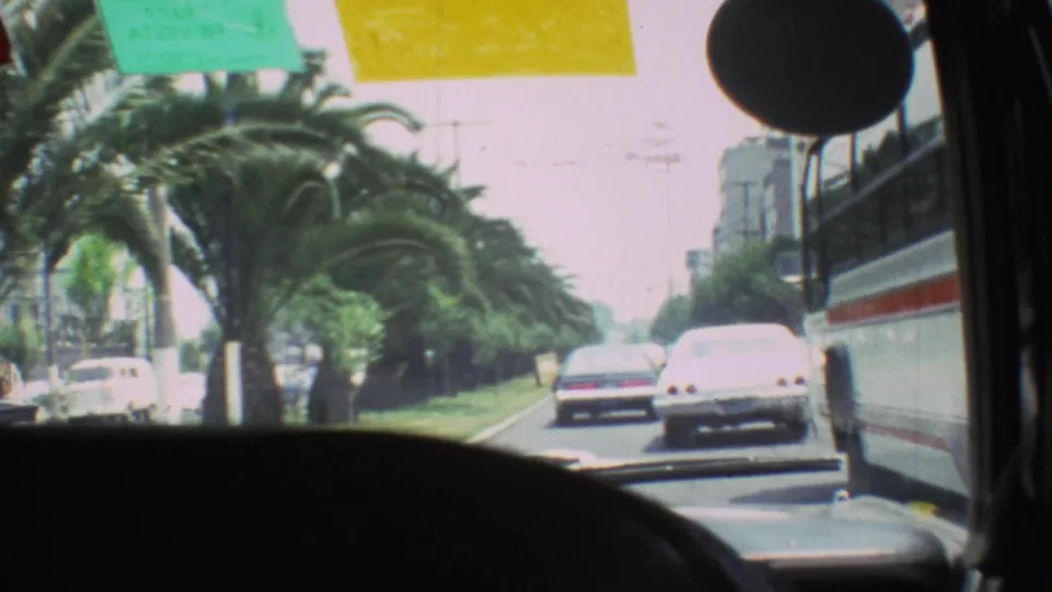 1973 Mexico City windshield view along a palm-lined road, with cars ahead, a white car, and a large vehicle at right.