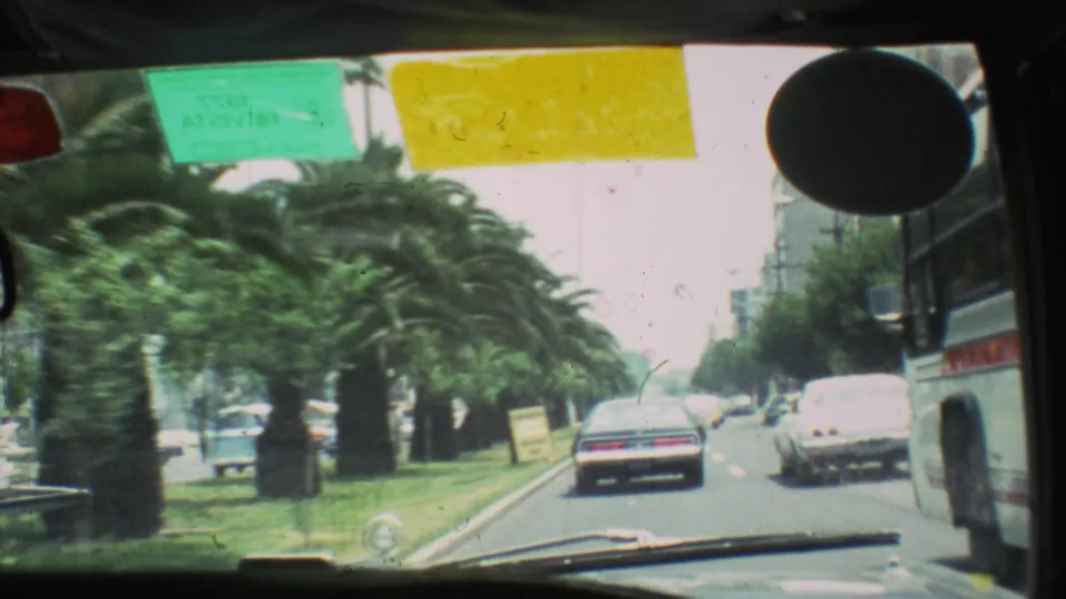 1973 Mexico City street-driving frame with cars, a bus along the right side, palm trees, and windshield permits visible.