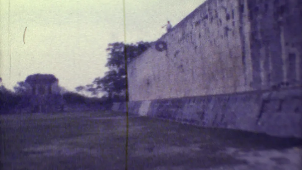 1973 Yucatan travel frame showing a long stone wall, open ground, trees, and a distant person standing along the top edge.
