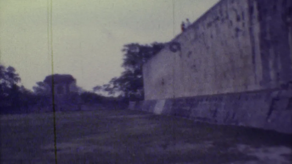 1973 Yucatan home-movie frame with the stone wall dominating the right side and a small structure beyond the courtyard.