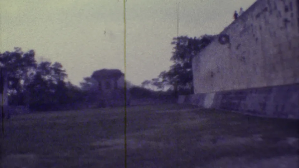 1973 Yucatan 8mm frame showing the courtyard more openly, with trees, distant masonry, and the wall entering at right.