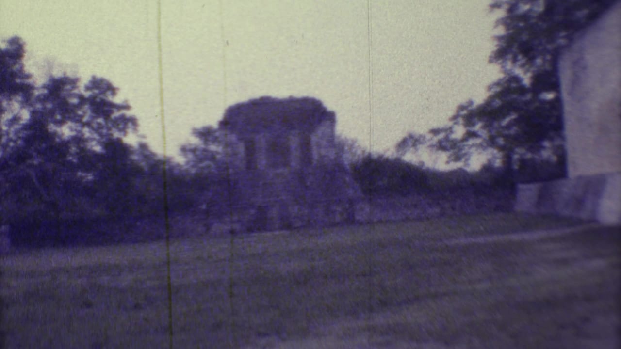 Wide view of a stone ruin partly surrounded by trees and grass.