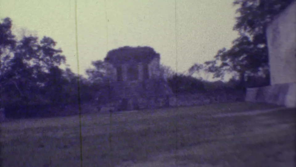 1973 8mm Yucatan footage showing a weathered Mayan ruin at a distance, with trees, grass, and visible film grain.