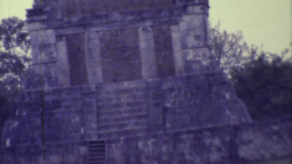 1973 8mm Yucatan close view of a weathered stone facade, stepped base, and dark lower opening with heavy purple film cast.