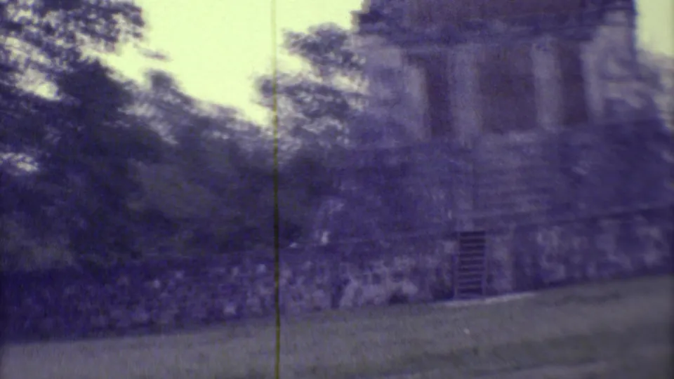1973 8mm Yucatan frame showing the ruin from a slightly angled handheld view, with grass, trees, and soft film texture.