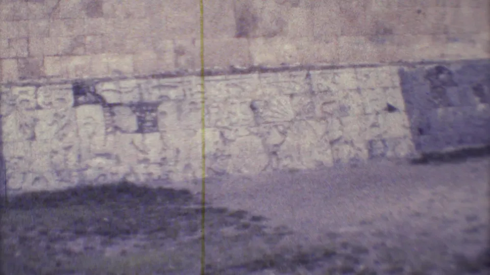 Closer 1973 Yucatan frame of weathered carved stonework on a ruin wall with grass at the base.