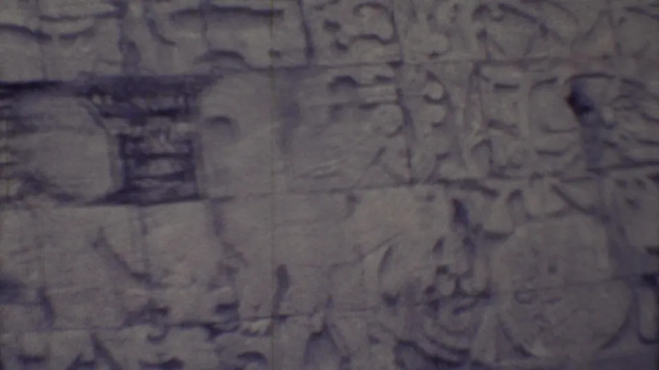 1973 Yucatan 8mm frame of a carved stone wall section with glyph blocks, relief details, and dark joints between stones.