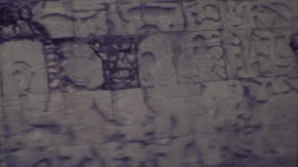 1973 Yucatan close-up of a weathered carved stone wall with glyph marks, partial relief figures, and visible 8mm scratches.