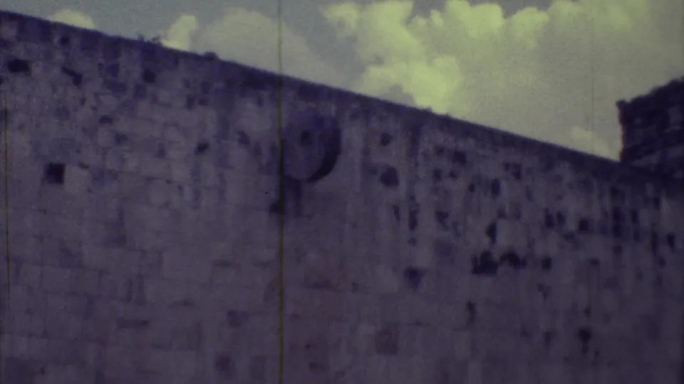 1973 Yucatan home-movie frame of a long stone ruin wall with small openings, faded color, and visible film wear.