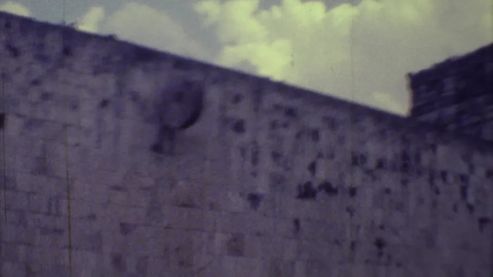 1973 Yucatan 8mm view of a massive weathered wall and raised corner structure seen from a visitor's handheld angle.