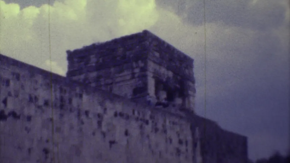 Handheld 1973 Yucatan footage frames the upper mass of a weathered stone ruin against a clouded sky.