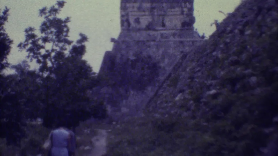 A woman in a light dress walks toward a stepped stone ruin amid foliage in 1973 Yucatan home-movie footage.