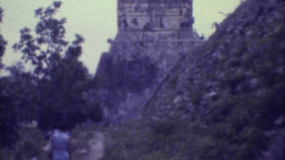 1973 8mm frame from Yucatan, Mexico, showing two women from behind on a jungle path approaching a large Maya pyramid.
