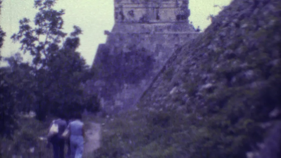 Yucatan, Mexico 1973 8mm frame showing visitors near the base of a vine-covered Maya pyramid, with trees framing the path.