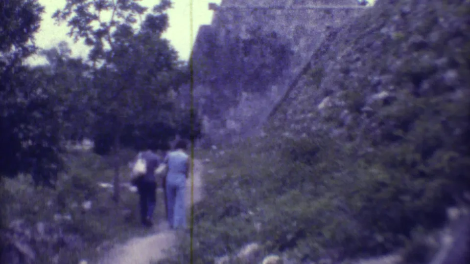 Two women walk away from the camera along a narrow path near stone ruins in Yucatan, Mexico, in 1973.
