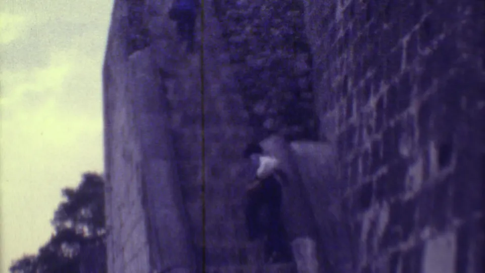 A visitor moves up the steep stone staircase, filmed close to the textured ruin wall in 1973 Yucatan footage.
