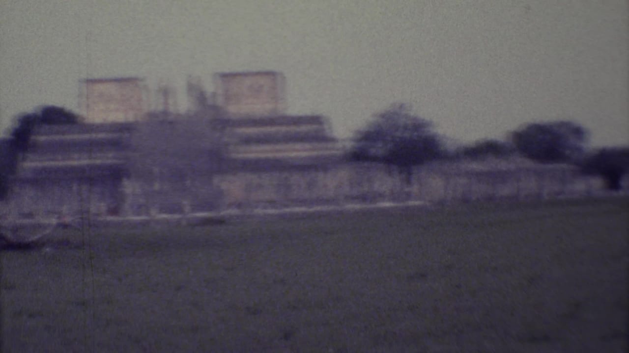 Distant stone ruins and trees across a grassy field under an overcast sky.