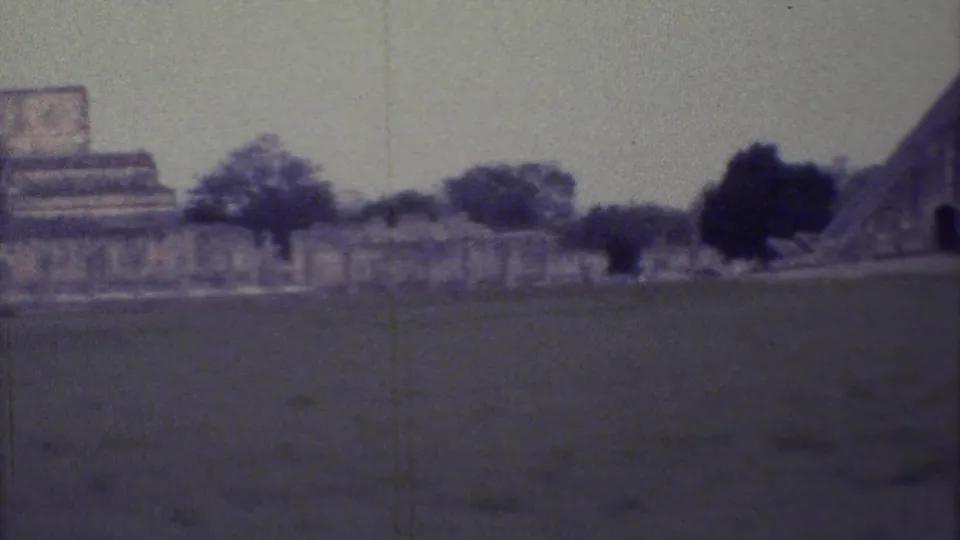 A handheld 8mm frame shows Yucatan stone ruins and trees across an open field, with faded color and visible film wear.