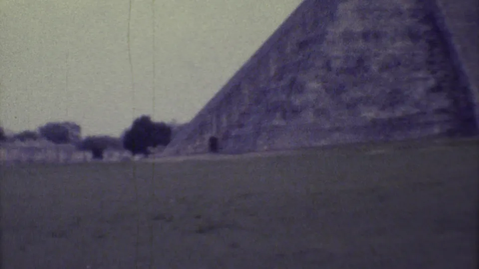 A large stepped pyramid dominates the right side of this 1973 Yucatan home-movie frame, with a dark entrance and grassy foreground.